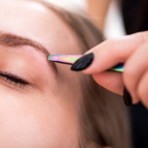 Plucking eyebrows with tweezer by beautician at beauty salon